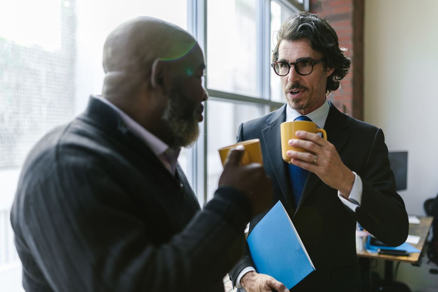 Two men in jackets talking with coffee in an office