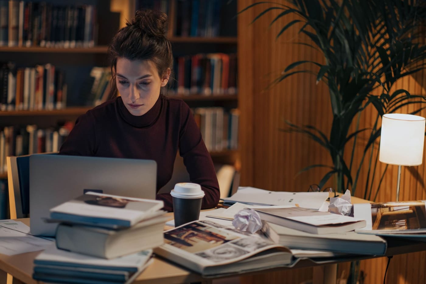 A woman at a desk with books, a laptop and a coffee cup