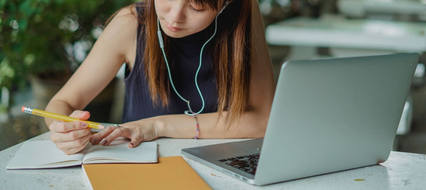 A young woman taking notes while studying at a laptop
