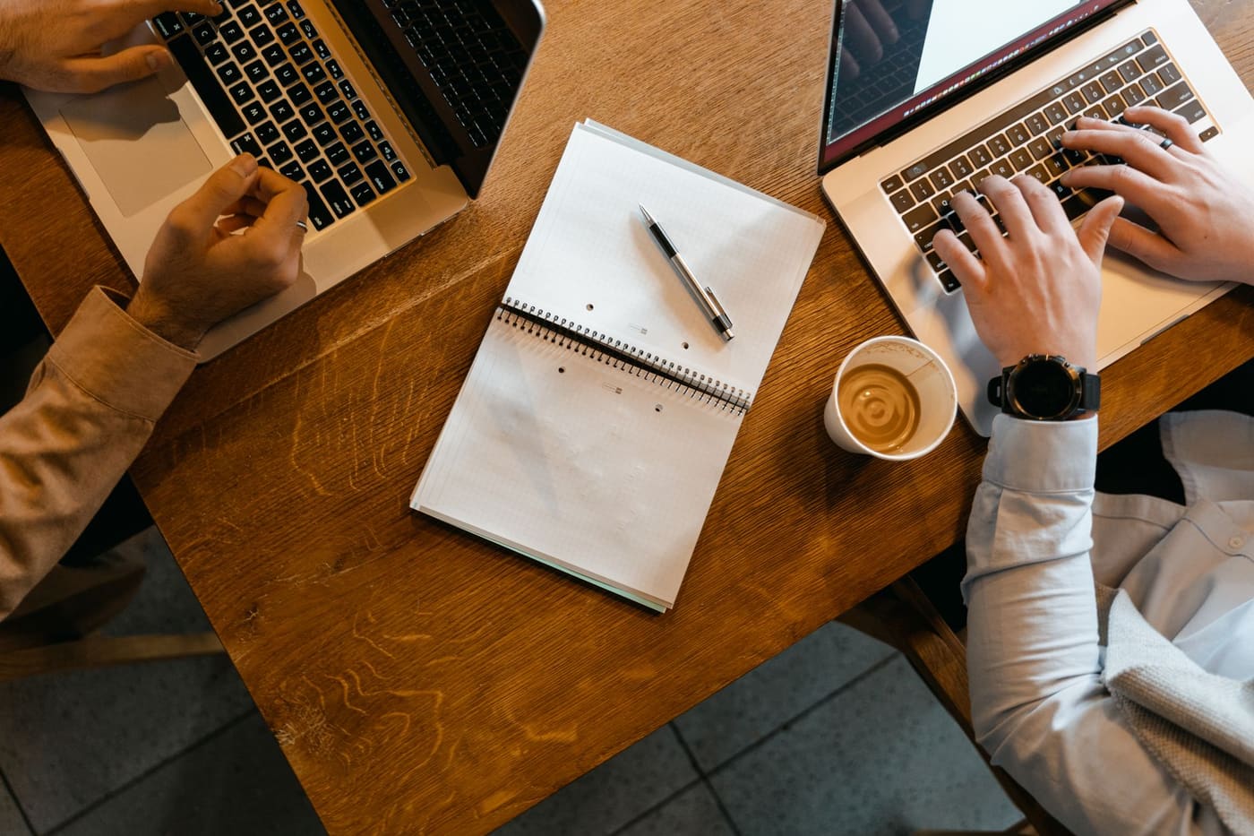 Overhead view of laptops, notes and coffee on a wooden desk