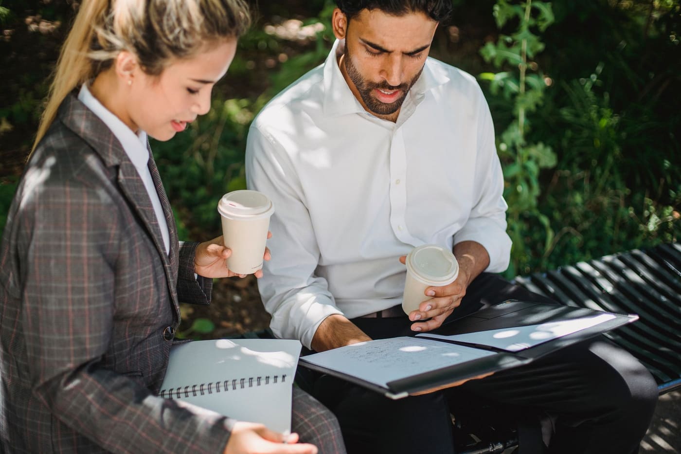 Two people reviewing documents with coffee on a park bench