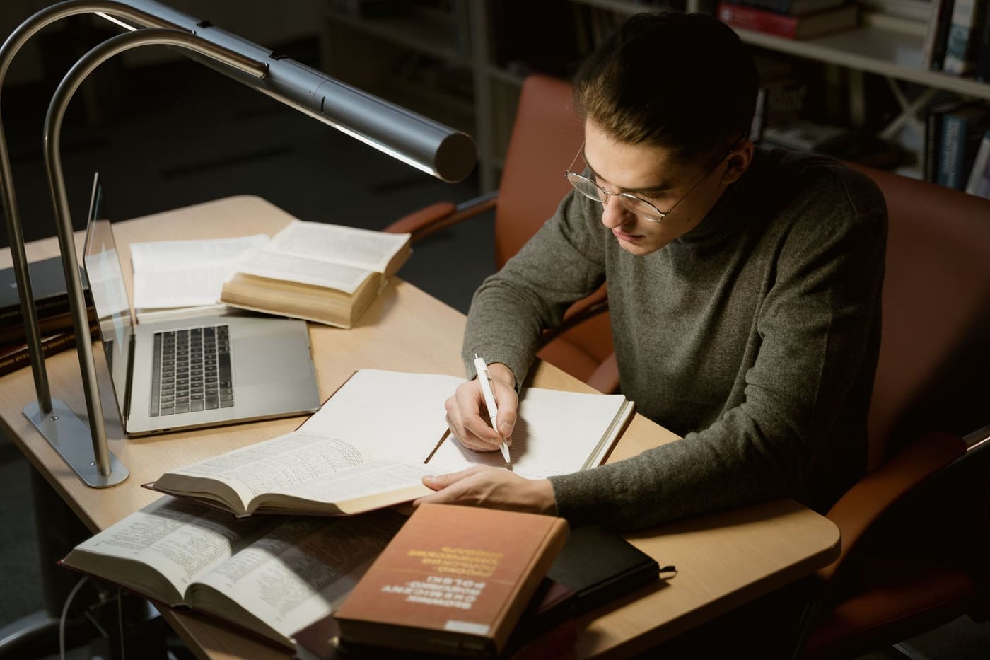 A young adult taking notes at a desk with books and a laptop