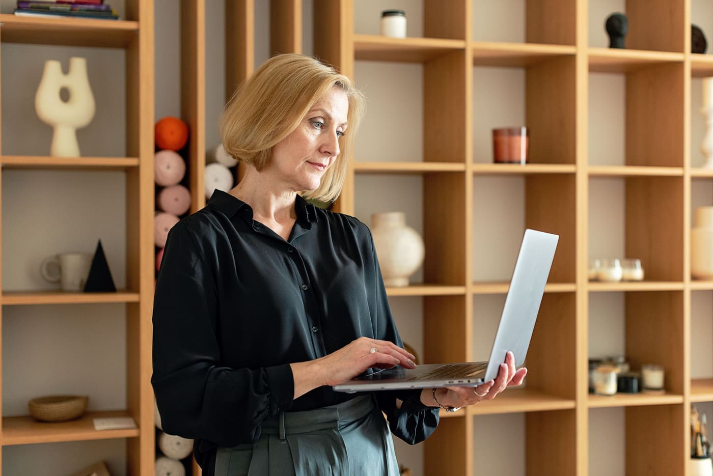 A woman holding an open laptop in front of wooden shelves