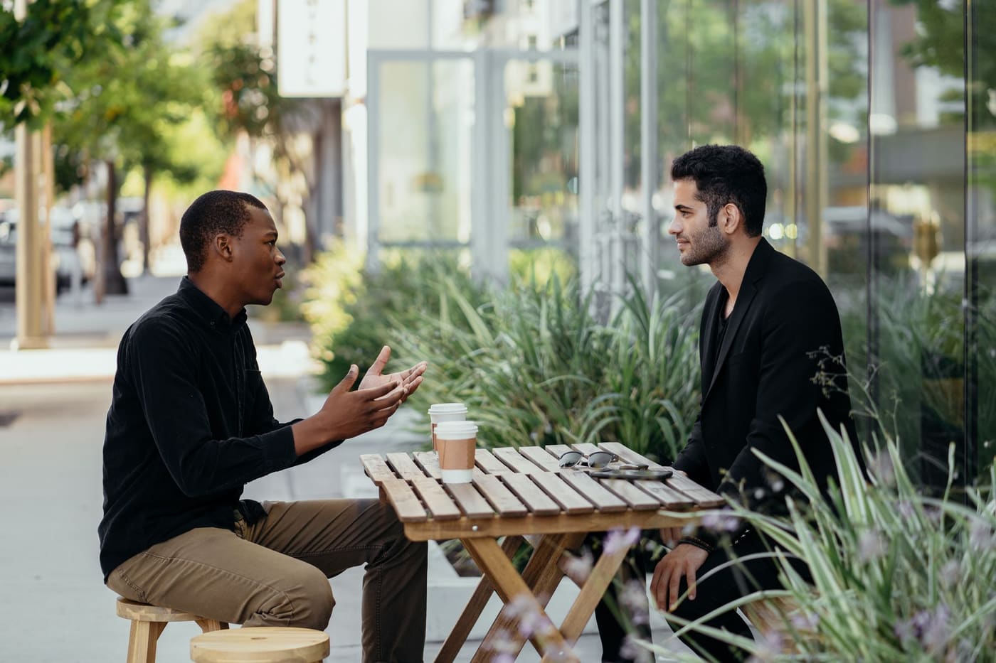 Two men in conversation at a small wooden table at an outdoor cafe