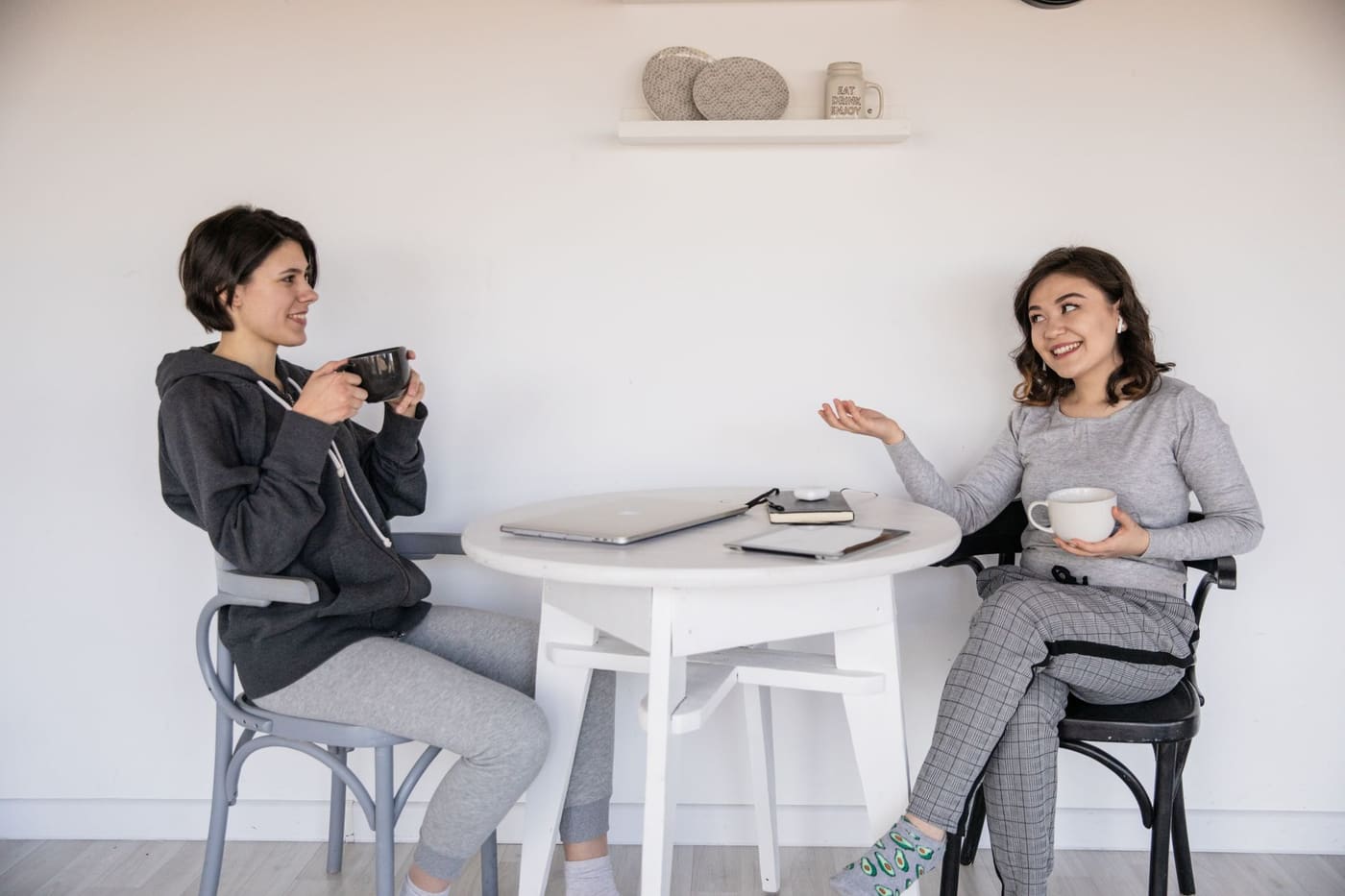 Two women talking and smiling over coffee at a small white table